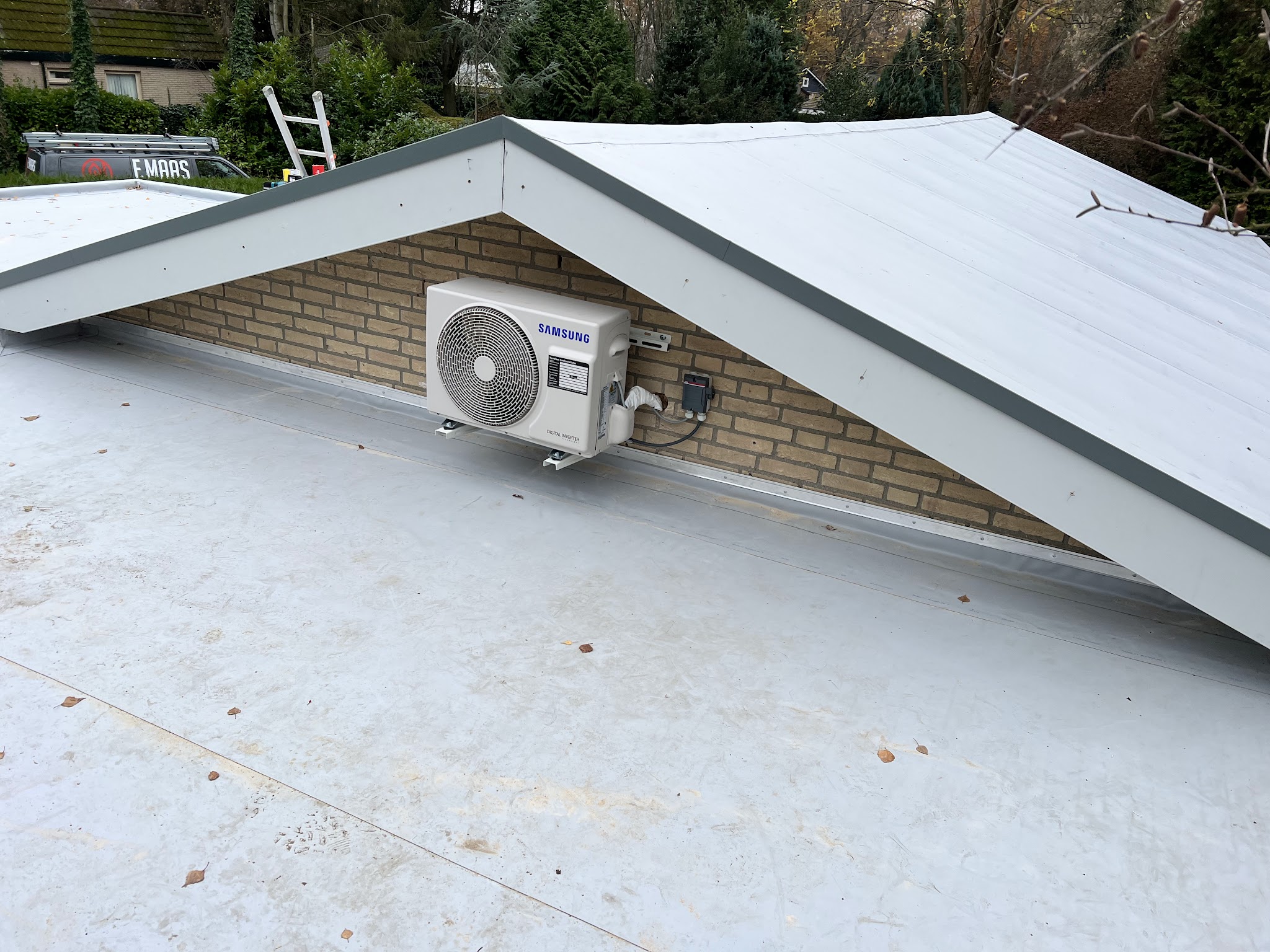 Nieuw wit kunststof dak met airco-buitenunit tegen een gevel onder een puntdak